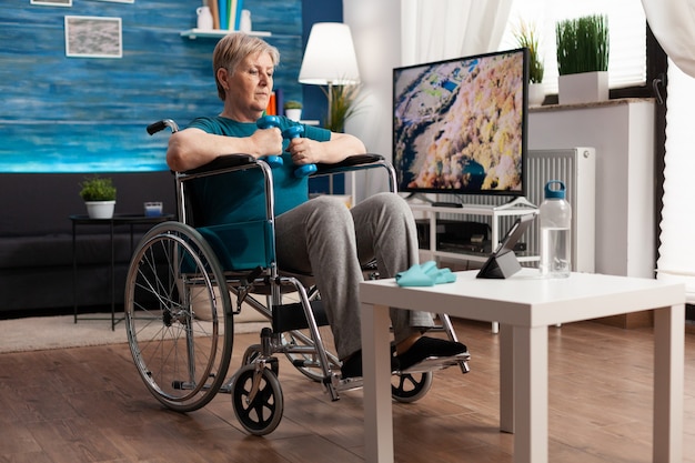 Ungültige ältere Frau im Rollstuhl trainiert Körpermuskeln mit gymnastischen Hanteln Erholung nach Lähmung