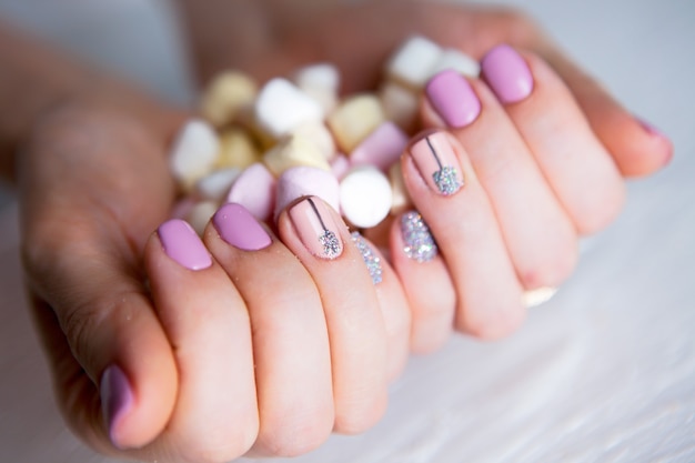 Unhas de glitter rosa com doces de marshmallow na mão de uma mulher. Manicure colorida e vívida em dedos de senhora e doces