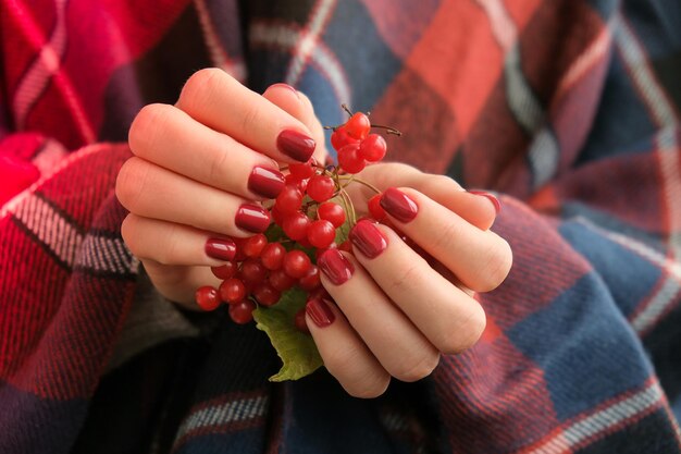 Unhas femininas vermelhas elegantes Mãos segurando groselhas modernas Linda manicure Outono inverno conceito de design de unhas de tratamento de beleza Unhas de gel Cuidados com a pele