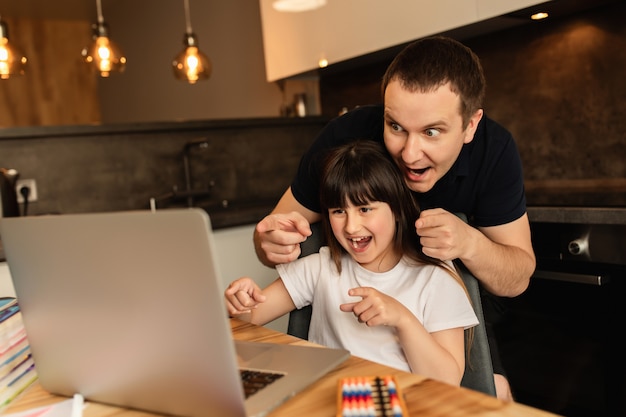 União familiar e aprendizado on-line. pai e filha fazem aula on-line com o laptop em casa