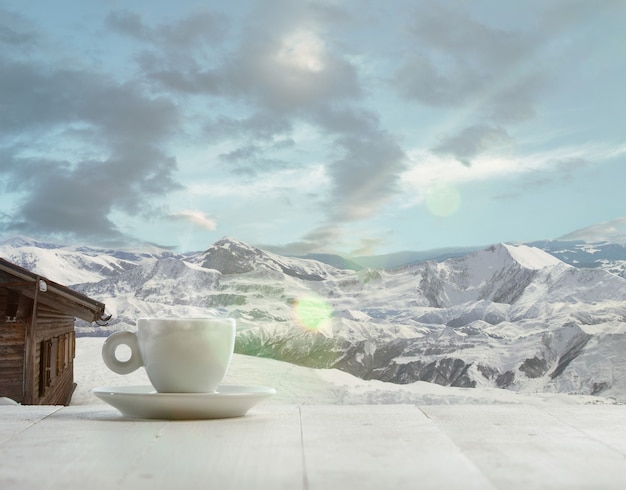 Única xícara de chá ou café e paisagem de montanhas no fundo. xícara de bebida quente com aparência de neve e céu nublado na frente dela. quente no dia de inverno, feriados, viagens, ano novo e época do natal.