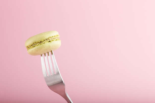 Único macaron verde ou bolo de biscoito em um garfo no fundo rosa pastel