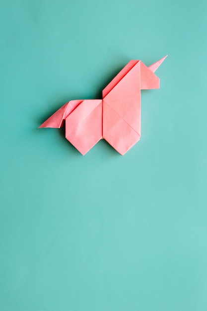 Foto unicórnio de origami rosa sobre fundo azul ciano