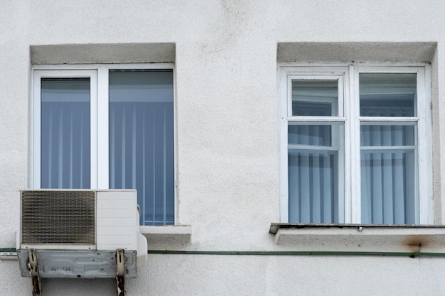 Una unidad de aire acondicionado exterior instalada en la pared de un edificio residencial junto a la ventana Instalación, reparación y mantenimiento de sistemas de aire acondicionado en locales residenciales