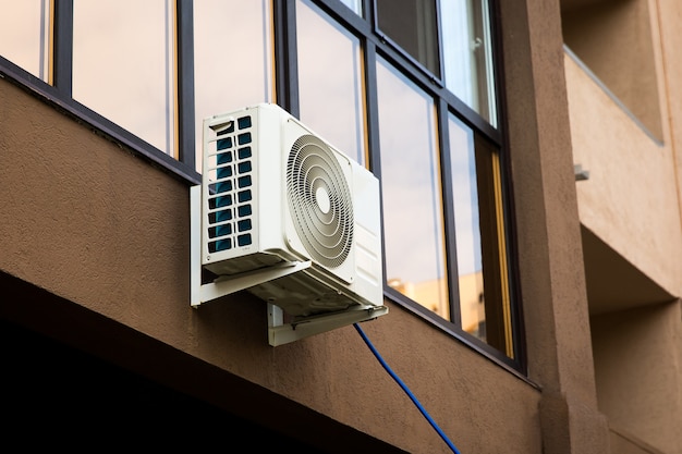 Unidad de aire acondicionado externo de metal gris en la pared marrón de la casa