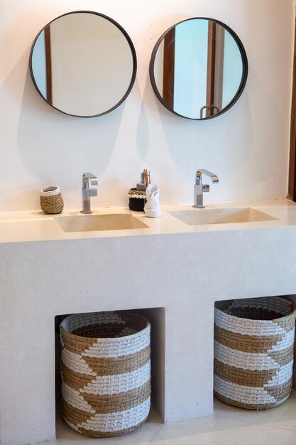 Unidade de vaidade moderna do banheiro com duas pias de concreto dois espelhos com moldura preta cestas de madeira natural