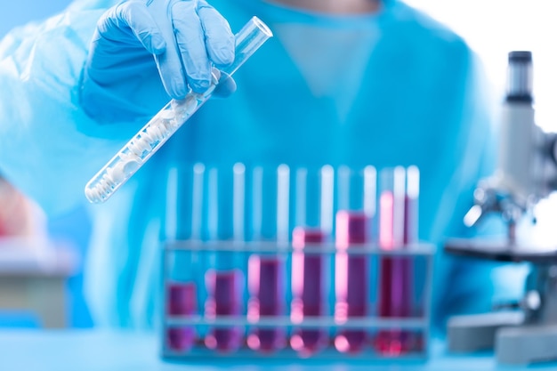 Uniforme de assistente de laboratório com luvas de máscara segurando tubo de ensaio com amostra de pesquisa de laboratório de ciências enquanto analisa o desenvolvimento em química de biologia à medida que o crescimento do gráfico aumenta o espaço de cópia da receita de investimento