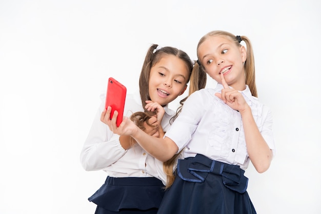 Uniforme escolar de meninas leva selfie smartphone. Posando para tirar uma foto perfeita. Lazer feminino. As meninas apenas querem se divertir. O penteado fofo das alunas usa o telefone celular ou smartphone para compartilhar fotos.