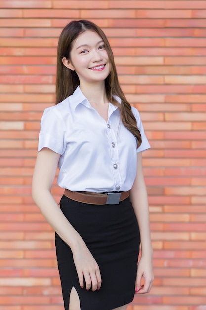 Uniforme de estudiante universitario Hermosa chica asiática de pie con su sonrisa sobre un fondo de ladrillo