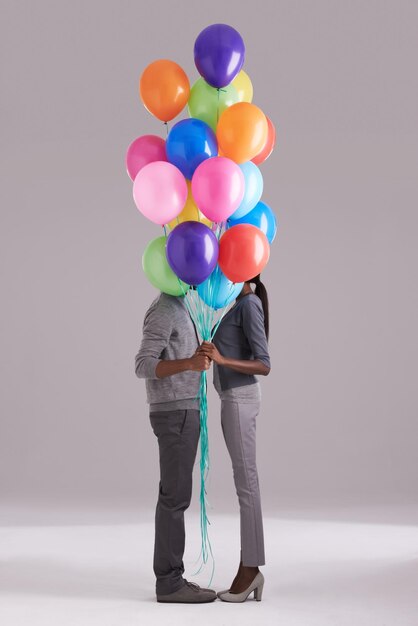 Unión detrás de globos Foto de estudio de una pareja escondida detrás de un montón de globos