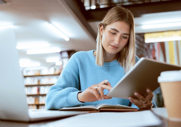 Foto universidade de educação e mulher na biblioteca com pesquisa de tablet e livros para projeto escolar ou exame laptop notebook e estudante universitário de internet estudando com tecnologia e e-learning no campus