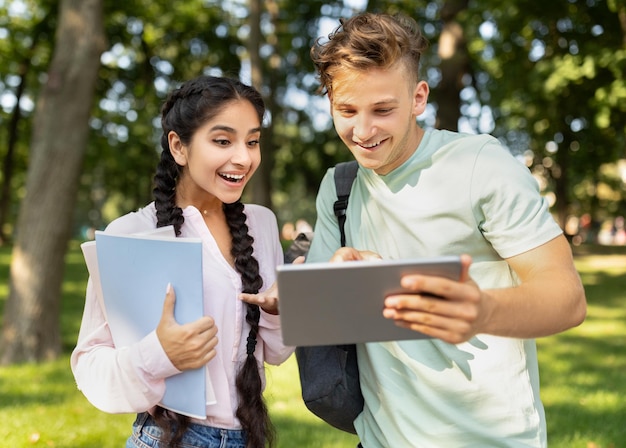 Universitäts-Lifestyle-Konzept-Student, der der Freundin, die sich den Test ansieht, ein digitales Tablet zeigt