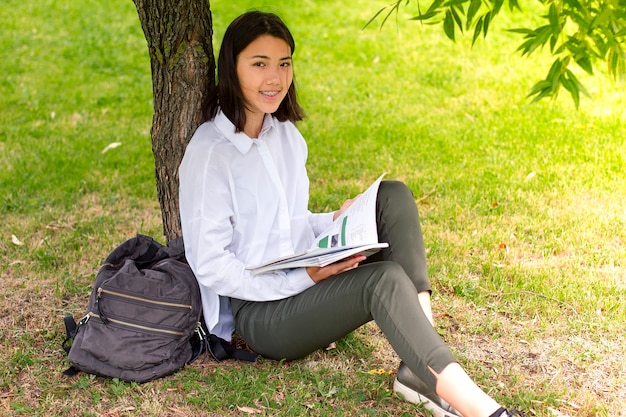 Universitätsmädchen, das Bücher oder Lehrbücher liest, die auf dem Gras sitzen