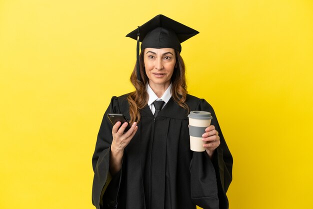 Universitário de meia-idade isolado em um fundo amarelo segurando um café para levar e um celular