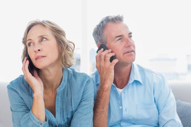 Unmmiling casal em seus telefones celulares no sofá