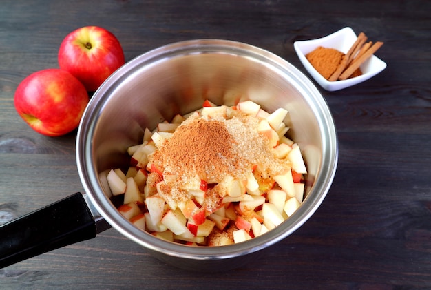 Unraffinierter Zucker und gemahlener Zimt, die in den Topf mit gewürfelten Äpfeln gegeben werden, um Apfelkompott zu machen