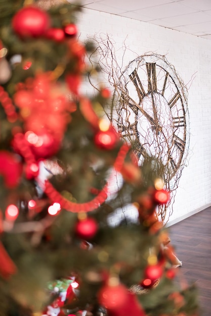 Foto unscharf geschmückter tannenbaum im vordergrund und eine große uhr an der wand im hintergrund