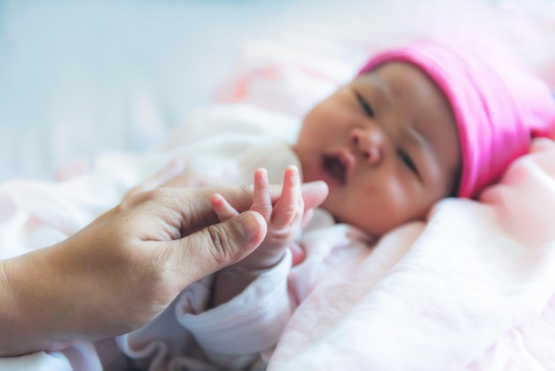 Unscharfe Bilder der Mutter hält die Hand einer neugeborenen Tochter, die 7 Tage alt ist und auf dem Bett liegt