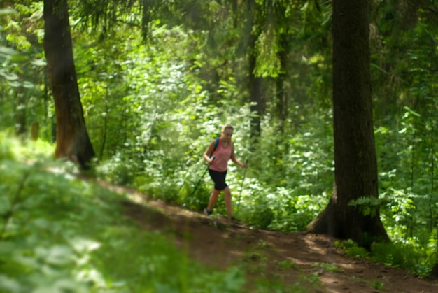 Unscharfer Hintergrund eines sonnigen Waldes, im Hintergrund die Umrisse einer wandernden Frau