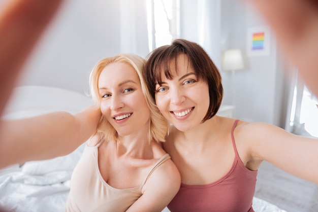 Unser Foto. Positive glückliche entzückte Frauen, die zusammen stehen und lächeln, während sie ein Selfie machen