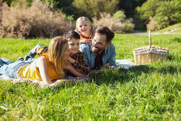 Unser picknick. fröhlicher bärtiger papa, der mit seiner familie lächelt und auf der decke liegt