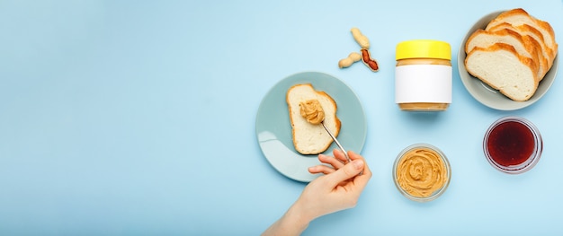 untar tostadas con mantequilla de maní, pasta de maní por manos femeninas sobre fondo azul. Proceso de cocción