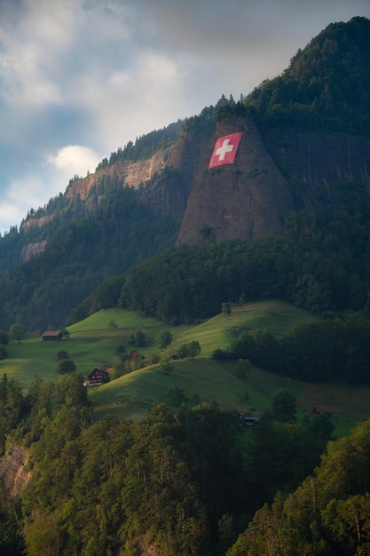 Unten an einer steilen Felswand hängt eine Schweizer Flagge, ein Bauernhof