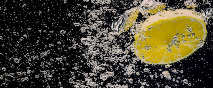 Foto unter wasser aus frisch gepresster, gesüßter limonade, die rohe zitronen in scheiben schneiden und in sodawasser vor dunkelblauem oder schwarzem hintergrund fallen. nahaufnahme von limonade oder kaltem erfrischungsgetränk mit highball-zitronencocktail