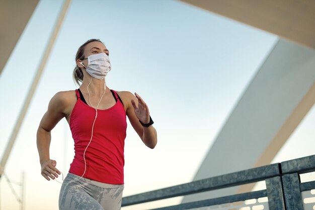 Unteransicht einer Läuferin, die mit schützender Gesichtsmaske im Freien joggt