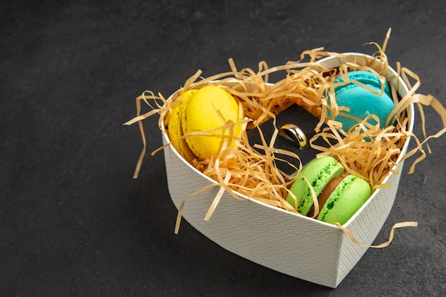 Unteransicht herzförmige Box mit Macarons Verlobungsring auf dunklem Hintergrund