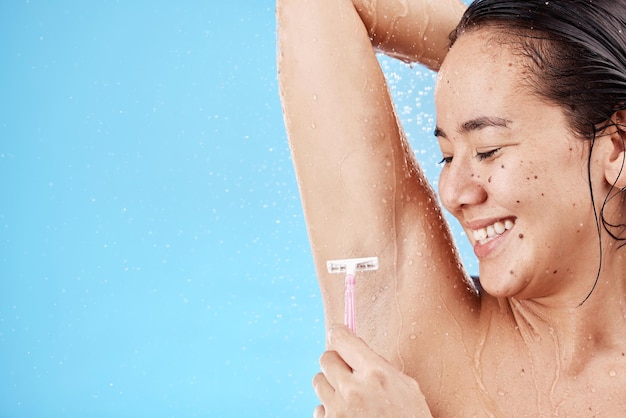 Unterarm duschen und sich mit einer vorbildlichen asiatischen Frau rasieren, die ihre Achselhöhle im Studio auf blauem Hintergrund zur Pflege rasiert Wasserluxus und Haarentfernung mit einer attraktiven jungen Frau im Badezimmer