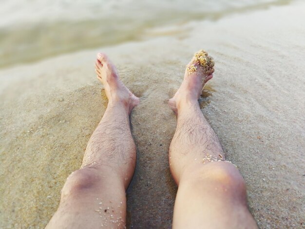 Foto unterer teil der beine einer person auf dem sand am strand