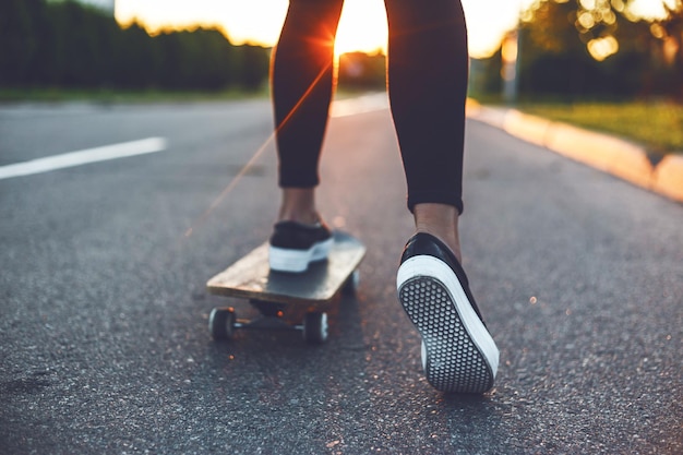 Unterer Teil einer Frau, die bei Sonnenuntergang auf der Straße Skateboard fährt