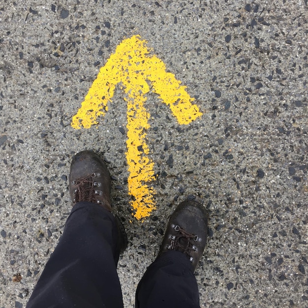 Foto unterer teil eines mannes, der an einem pfeilsymbol auf der straße steht