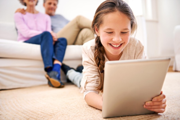 Unterhalten, wo immer sie ist Aufnahme von Großeltern, die ihrer Enkelin beim Umgang mit einem digitalen Tablet zusehen