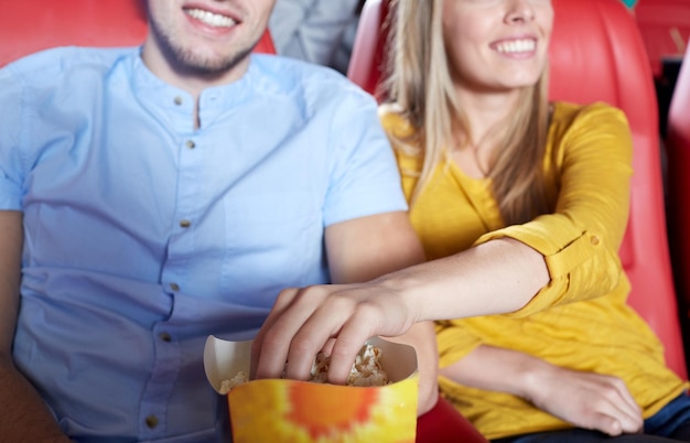 Unterhaltungs-, Freizeit- und People-Konzept - Nahaufnahme eines glücklichen Paares, das Filme anschaut und Popcorn im Theater oder Kino isst