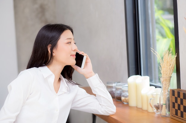 Unterhaltungstelefon und -lächeln der schönen jungen asiatischen Frau in der Kaffeestube.