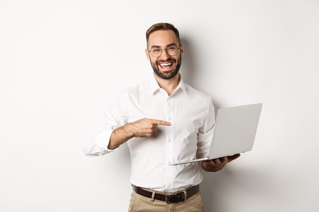 Unternehmen. Hübscher Manager mit Brille, der am Laptop arbeitet, auf den Computer zeigt und zufrieden lächelt, auf weißem Hintergrund stehend