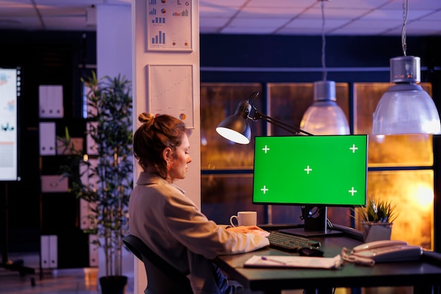 Unternehmer, der sich einen Green-Screen-Chroma-Key-Mock-up-Computer mit isoliertem Display ansieht und Überstunden an der Unternehmensstrategie im Startup-Büro arbeitet. Junger Manager, der das Wachstum des Finanzberichts analysiert