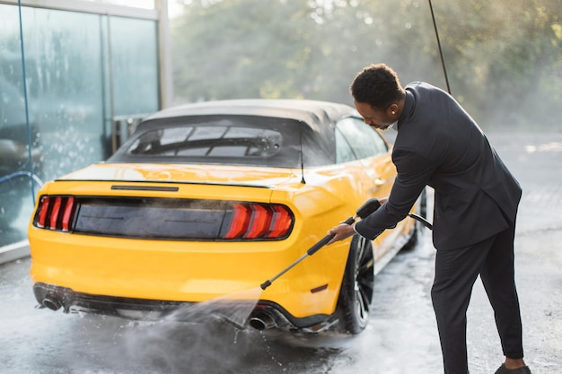Unternehmer im Business-Anzug wäscht sein gelbes Auto manuell zurück