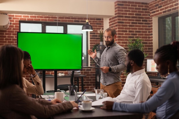 Unternehmer-Mann, der vor Mock-up-Chroma-Key-Monitor mit grünem Bildschirm steht, mit isolierter Anzeige, die die Partnerschaftsstrategie erklärt, die im Startup-Büro arbeitet. Konzept der Geschäftsleute bei der Arbeit