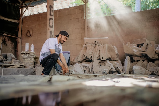 Unternehmer mit Hut schneidet Steinhandwerk mit Schneidwerkzeugen in der Werkstatt