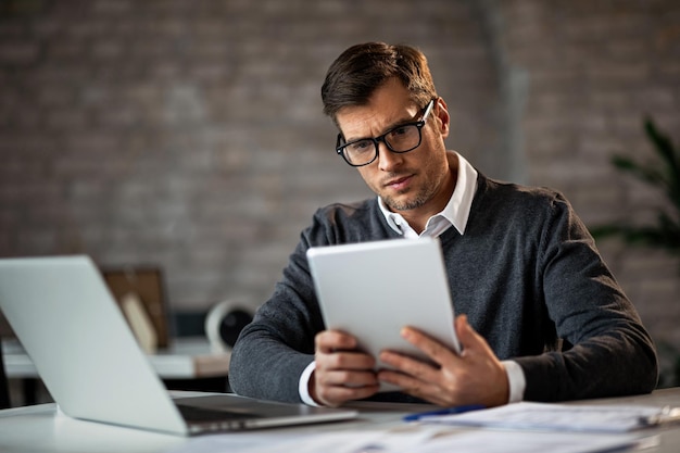 Unternehmer mittleren Alters, der an seinem Schreibtisch arbeitet und ein digitales Tablet verwendet