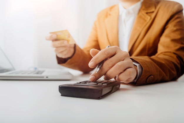 Unternehmerin, die einen Taschenrechner mit einem Stift in der Hand verwendet, um die finanziellen Ausgaben im Home Office zu berechnen