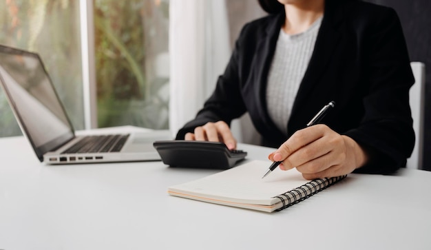 Unternehmerin, die einen Taschenrechner mit einem Stift in der Hand verwendet, um die finanziellen Ausgaben im Home Office zu berechnen