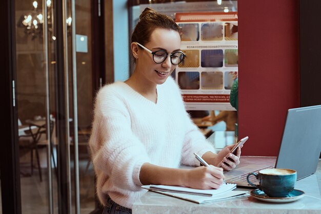 Unternehmerin, die vom Café arbeitet und am Handy mit Kopfhörern spricht