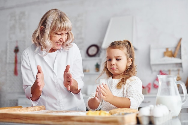 Unterrichtsprozess Ältere Großmutter mit ihrer kleinen Enkelin kocht Süßigkeiten für Weihnachten in der Küche