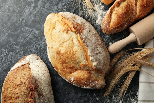 Unterschiedliches Brot, Ährchen und Nudelholz auf schwarzem rauchigem Hintergrund