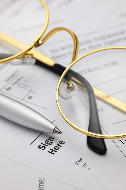Unterschreiben Sie hier das Wort auf Geschäftsdokumenten mit Brille und Kugelschreiber. Unterschrift oder Vertragskonzept