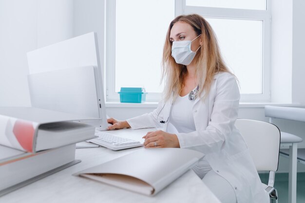 Untersuchung in einer modernen Klinik Eine Ärztin mit medizinischer Maske gibt die Untersuchungsdaten des Patienten in einen Computer ein